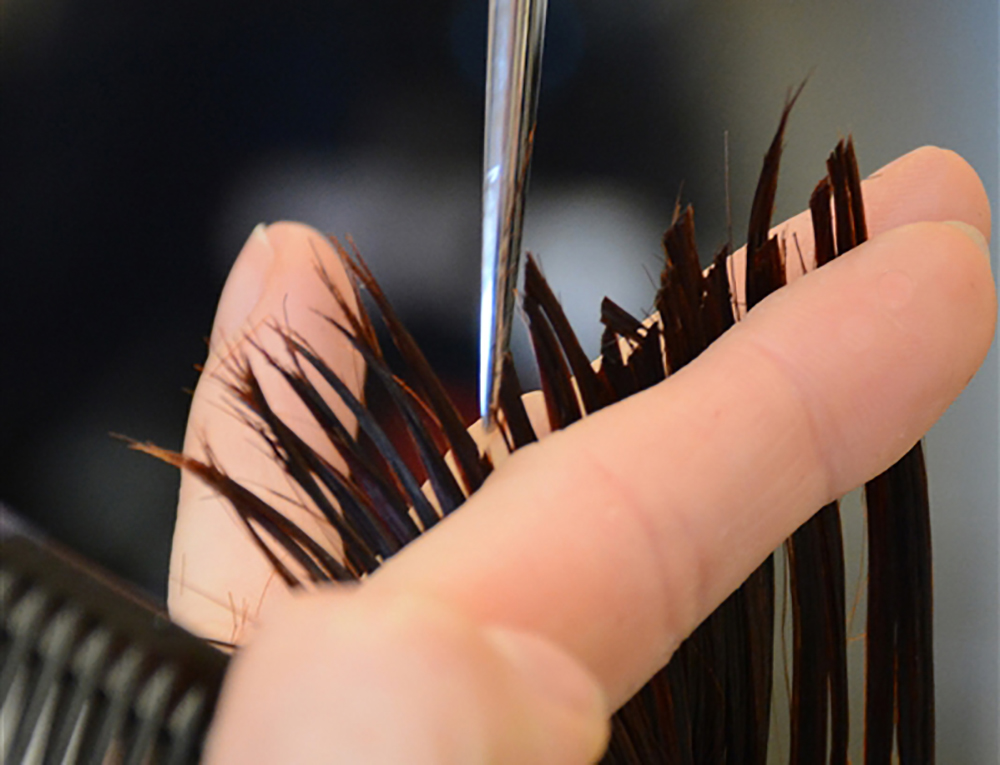 Haarsträhne zwischen den Fingern wird gerade geschnitten